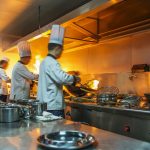 Bucatar in bucataria restaurantului la aragaz cu tigaie, facand flame pe mancare